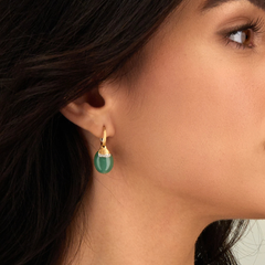  Um luxuoso brinco de ouro adornado com diamantes cintilantes e uma pedra de aventurina proeminente, exibindo uma mistura de opulência e beleza natural enquanto pende elegantemente de uma orelha de uma mulher com cabelo castanho escuro