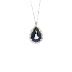 colar com um pingente que apresenta uma grande safira em forma de lágrima no centro, cercada por um halo de pequenos diamantes. A safira tem um tom azul profundo com reflexos de azul mais claro, indicativo de sua alta qualidade. O pingente está montado em uma configuração de ouro que também é incrustada com diamantes menores, adicionando ao brilho e luxo da peça. Acima da safira principal, há outro diamante singular preso à corrente de ouro do colar, que parece ser feita de ouro de ligação fina