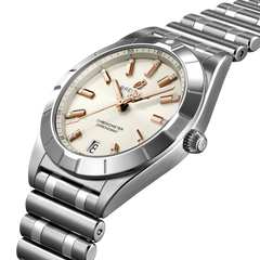 Relógio de pulso Breitling em aço inoxidável, apresentando uma pulseira e caixa prateadas. O mostrador do relógio é branco com marcadores de hora e ponteiros em tom de ouro rosa, e uma janela de data na posição das 3 horas. A marca “BREITLING” está escrita abaixo do marcador das 12 horas, com “CHRONOMETER” e “CERTIFIED” acima do marcador das 6 horas. Há marcadores de minutos ao redor da borda externa do mostrador.